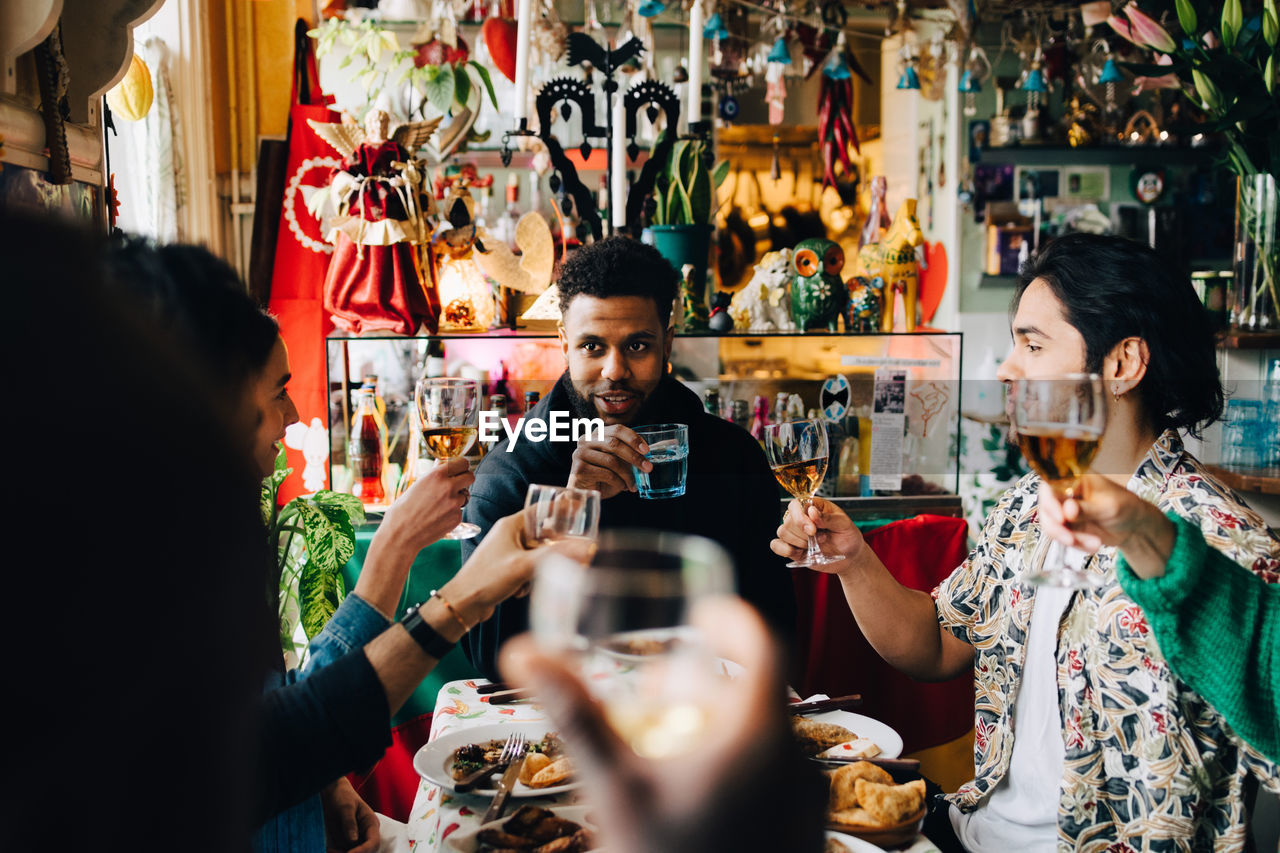 Cheerful young multi-ethnic friends raising toast while sitting at table in restaurant