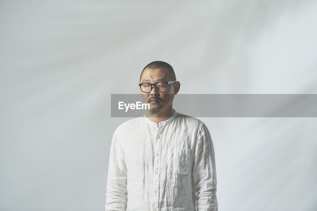 Man standing with eyes closed against white background