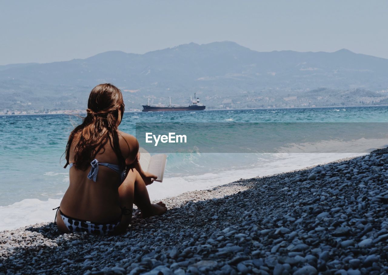 Rear view of woman reading on beach