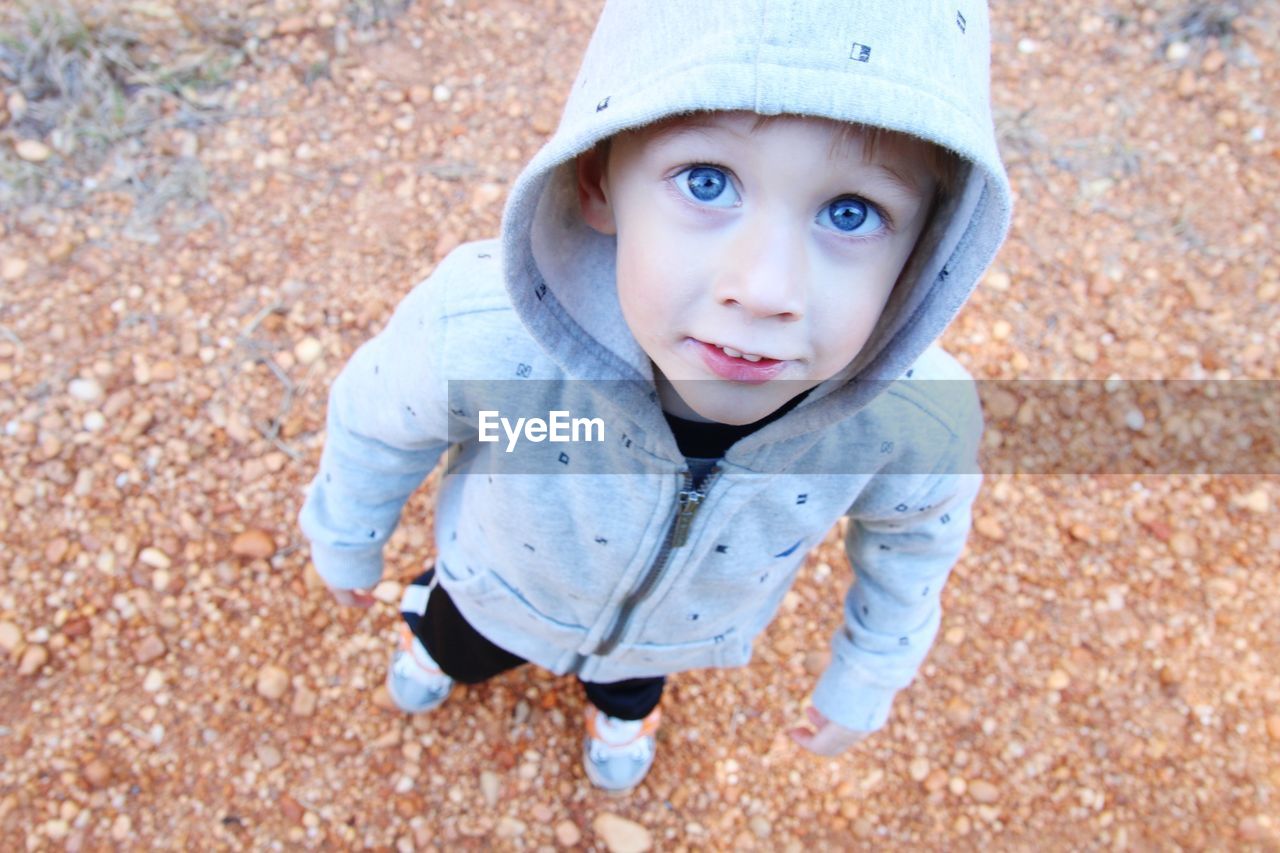 High angle view of cute boy wearing hooded jacket standing at park