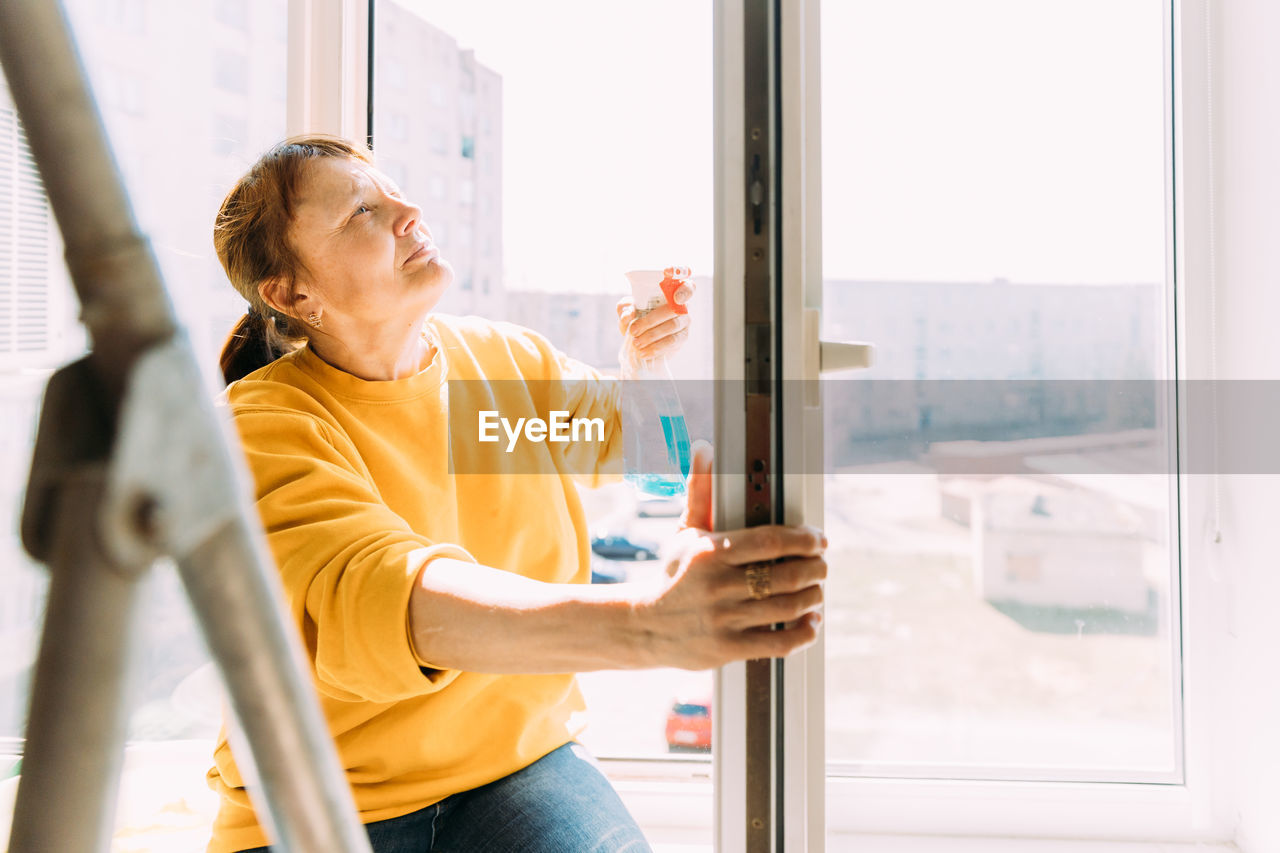 50 year old woman cleans windows from stains using rag and spray cleaner. 