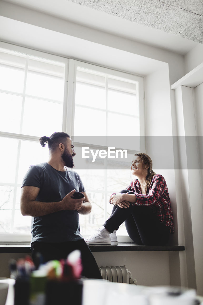 Low angle view of smiling engineers talking at window in creative office