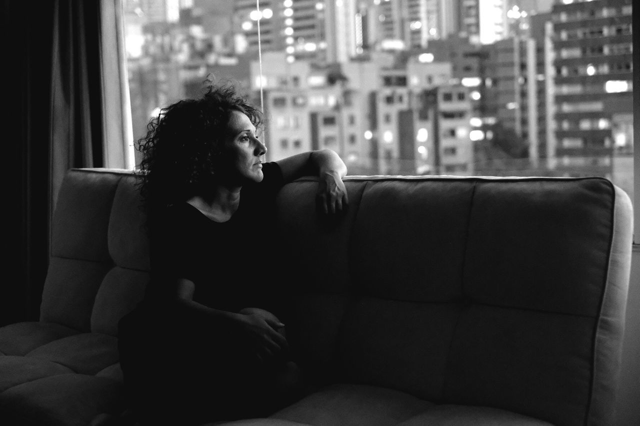 Woman sitting on sofa while looking through window in hotel