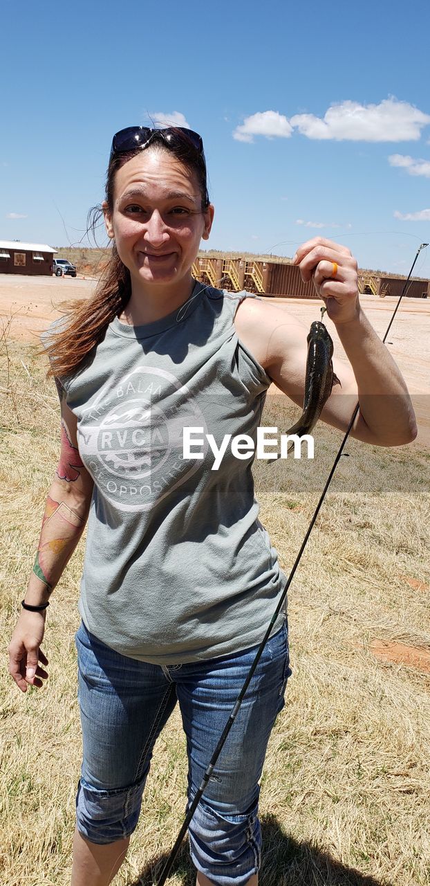 Portrait of smiling woman holding fish in fishing line on field during sunny day