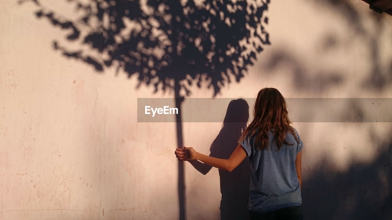 Optical illusion on woman holding tree shadow on wall