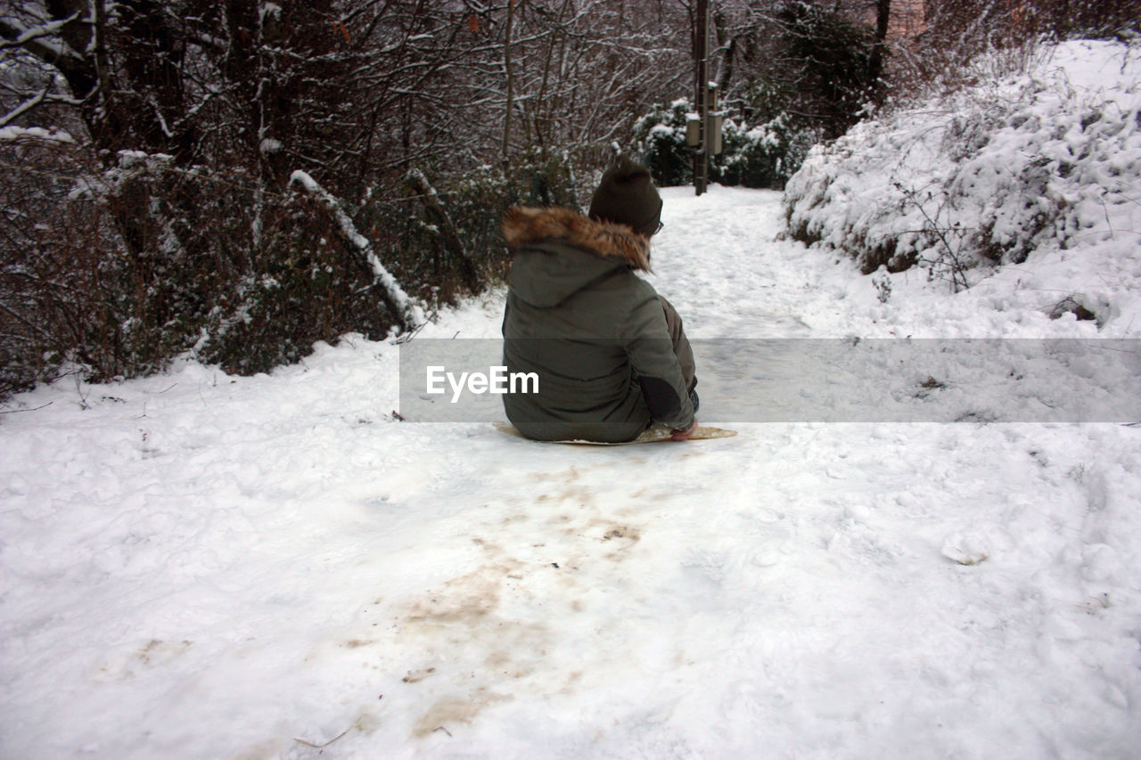 REAR VIEW OF MAN SITTING ON SNOW