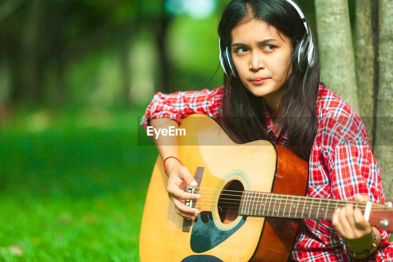 Young woman playing guitar while sitting at park