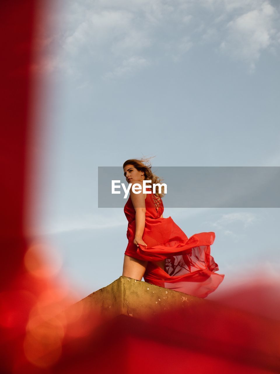 Low angle view of young woman wearing red dress against sky