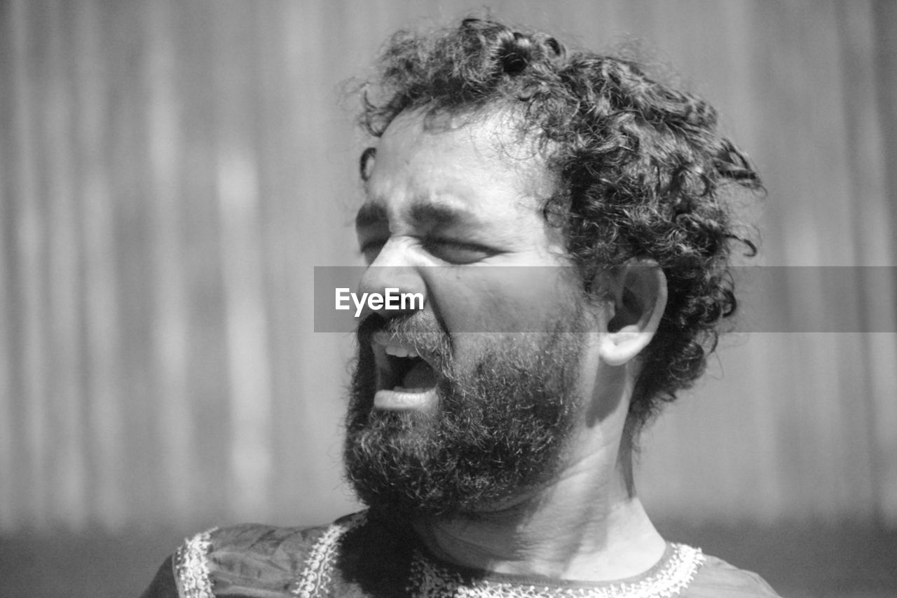 headshot, black and white, one person, portrait, adult, black, monochrome photography, monochrome, facial hair, beard, men, person, white, emotion, indoors, focus on foreground, close-up, human face, looking, hairstyle, lifestyles, mouth open, eyes closed, looking away, negative emotion, curly hair