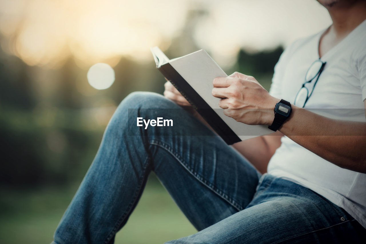 MIDSECTION OF MAN USING MOBILE PHONE WHILE SITTING ON CAMERA