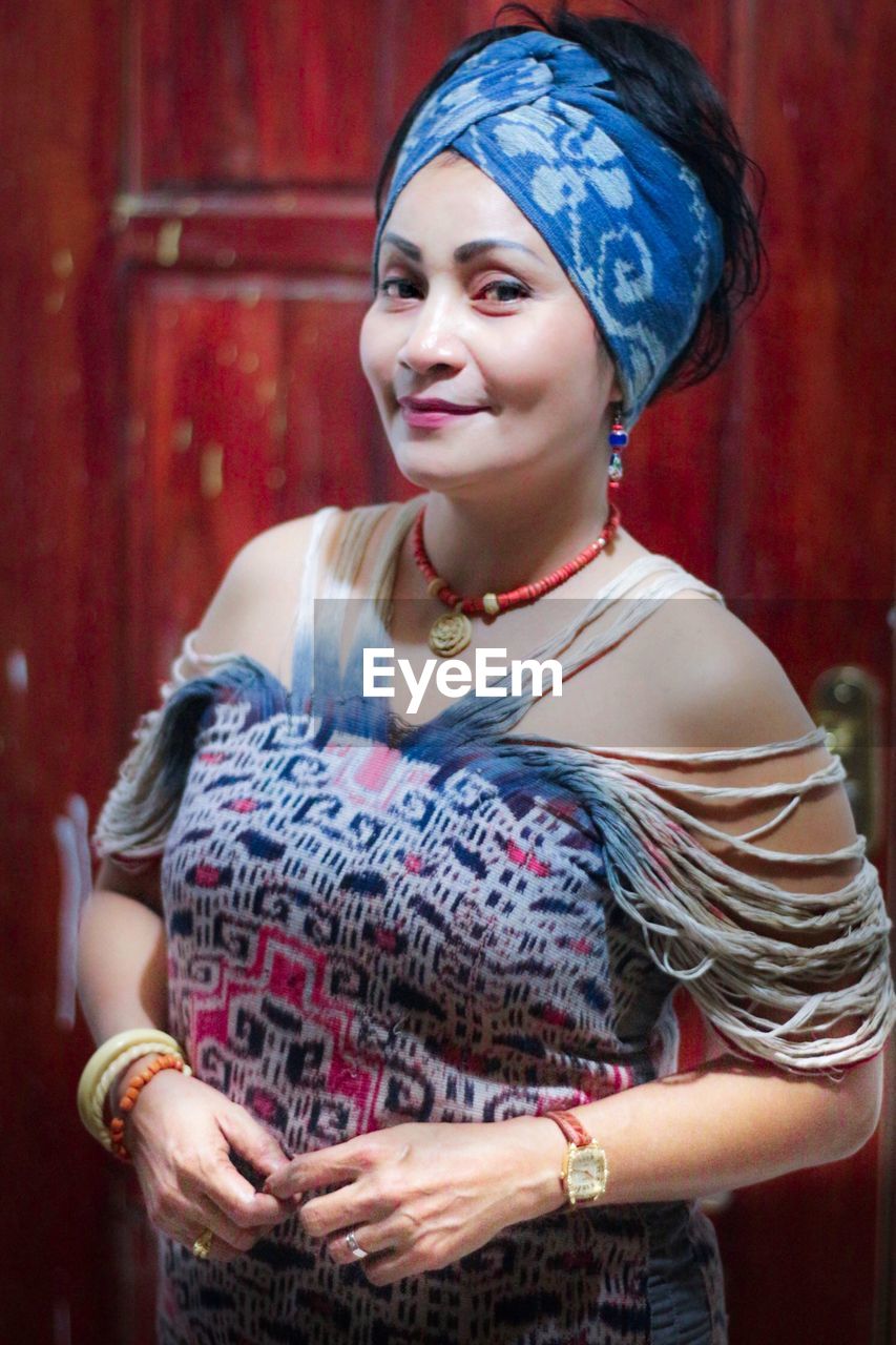 Portrait of smiling woman in traditional clothes standing against wall