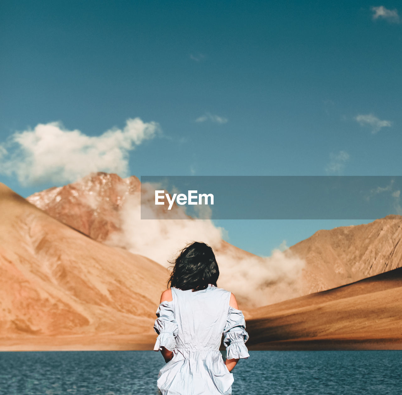 Rear view of woman standing by lake against mountain and sky