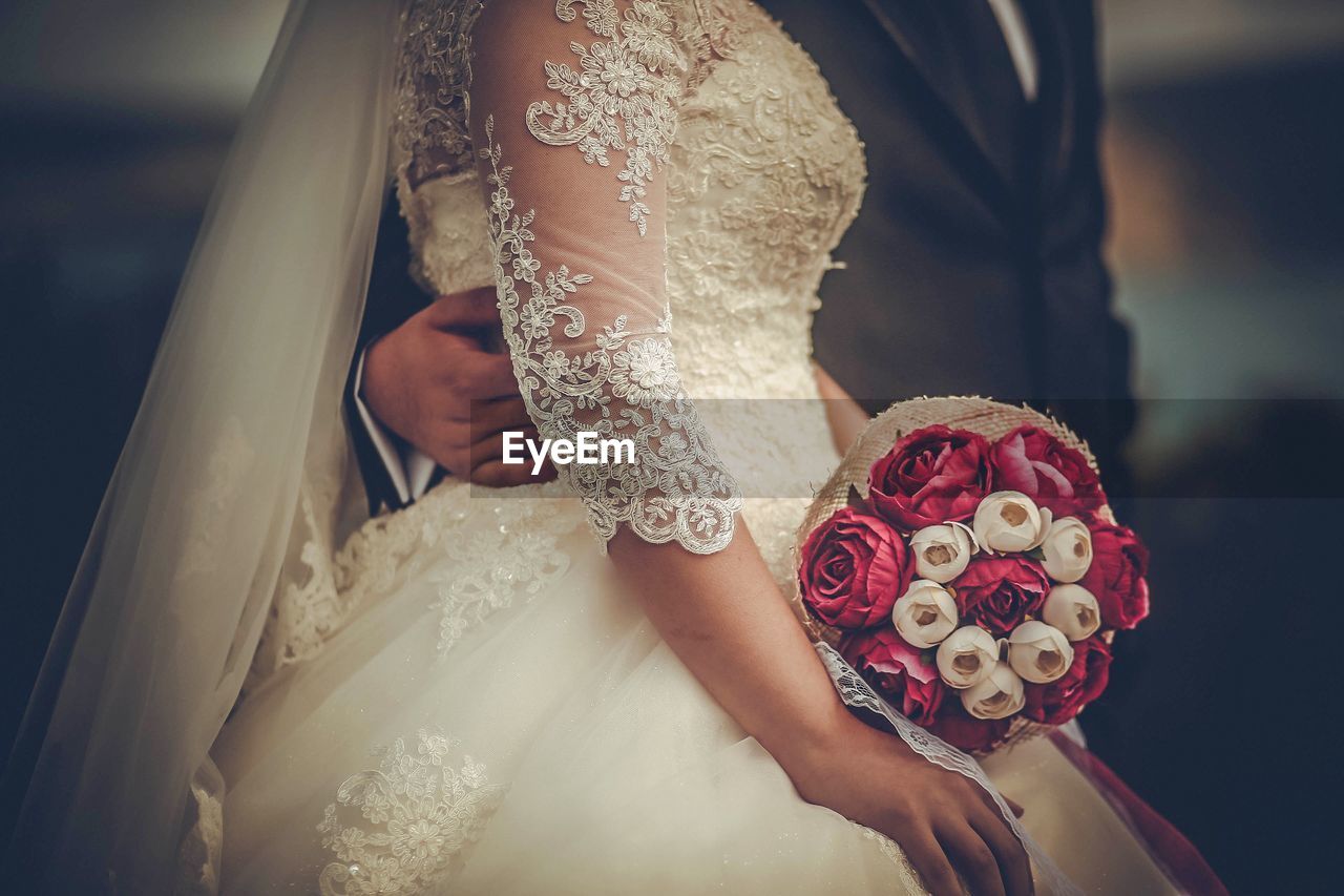 Midsection of bride holding bouquet with groom