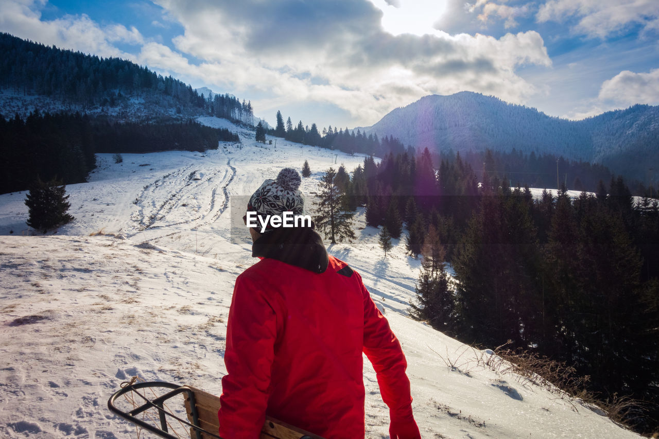 REAR VIEW OF MAN ON SNOWCAPPED MOUNTAIN AGAINST SKY