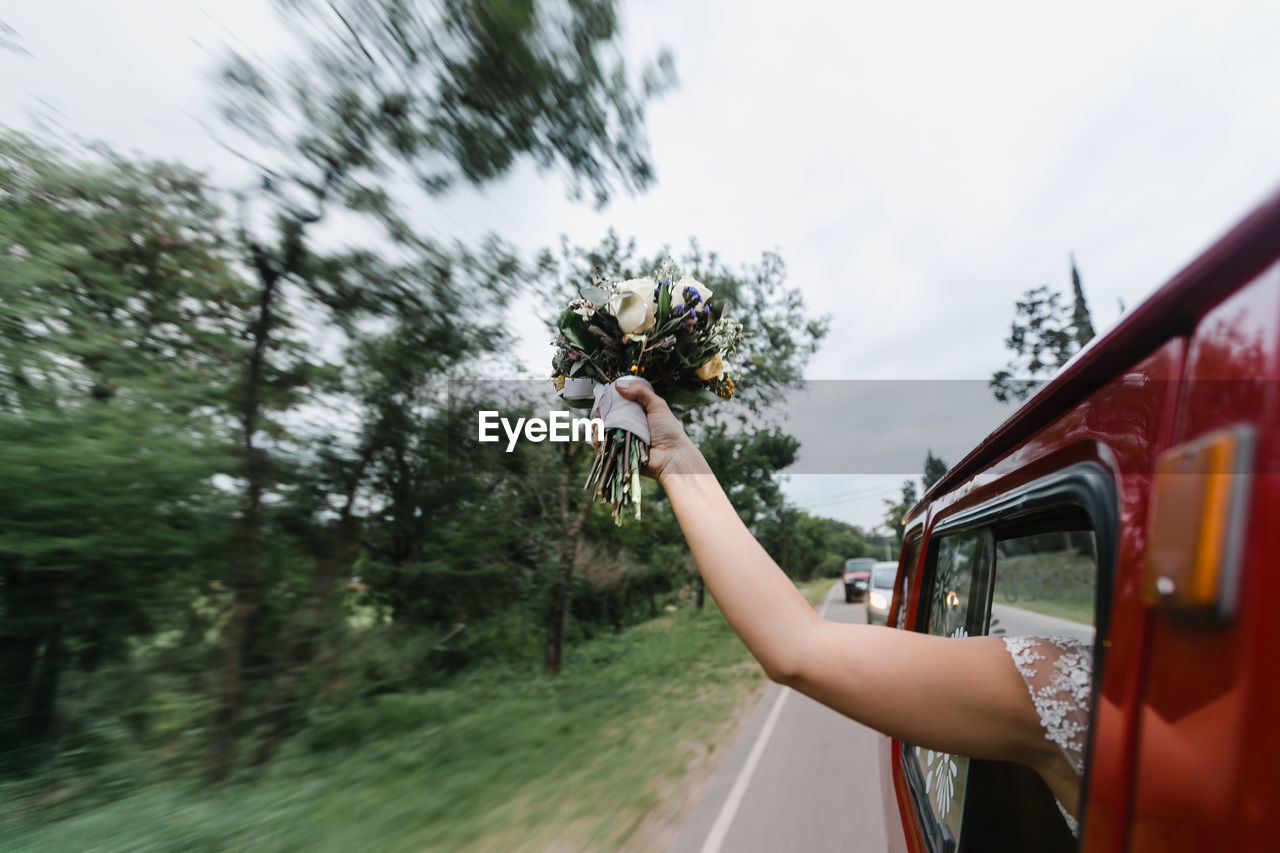 Cropped hand of bride holding bouquet through car window