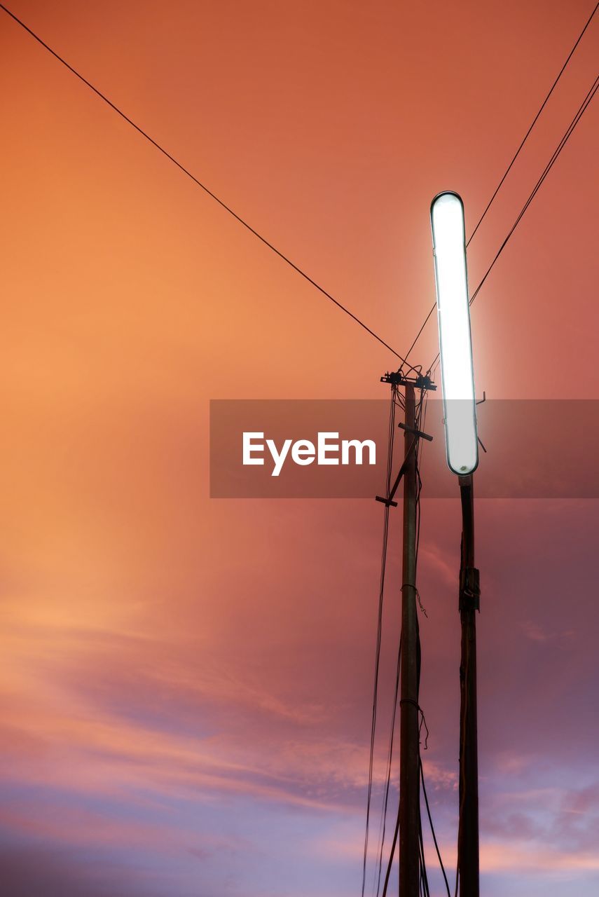 LOW ANGLE VIEW OF SILHOUETTE ELECTRICITY PYLONS AGAINST ORANGE SKY