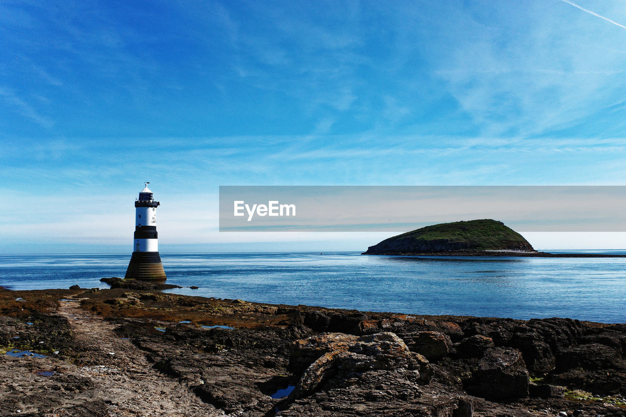 LIGHTHOUSE AMIDST ROCKS ON SEA AGAINST SKY