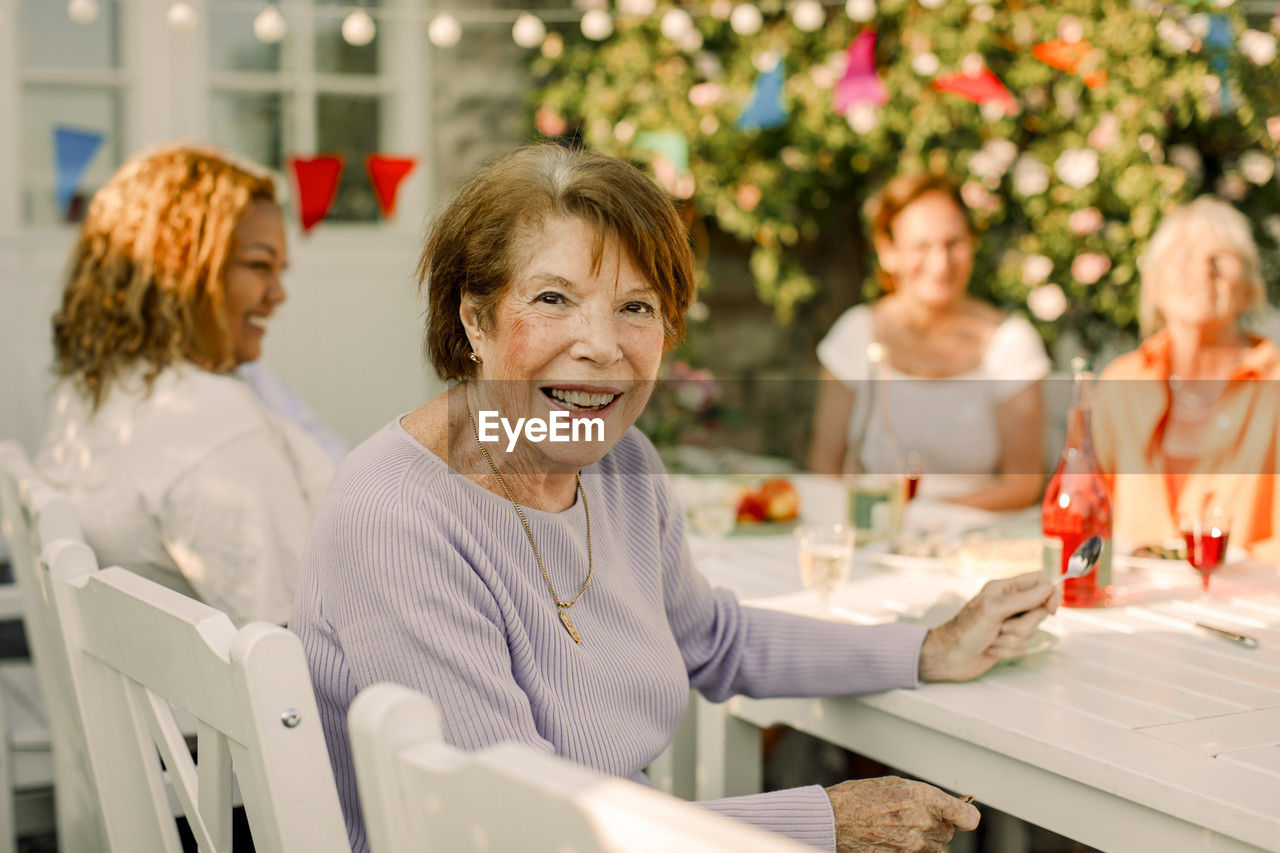 Portrait of happy senior woman sitting at dining table in back yard