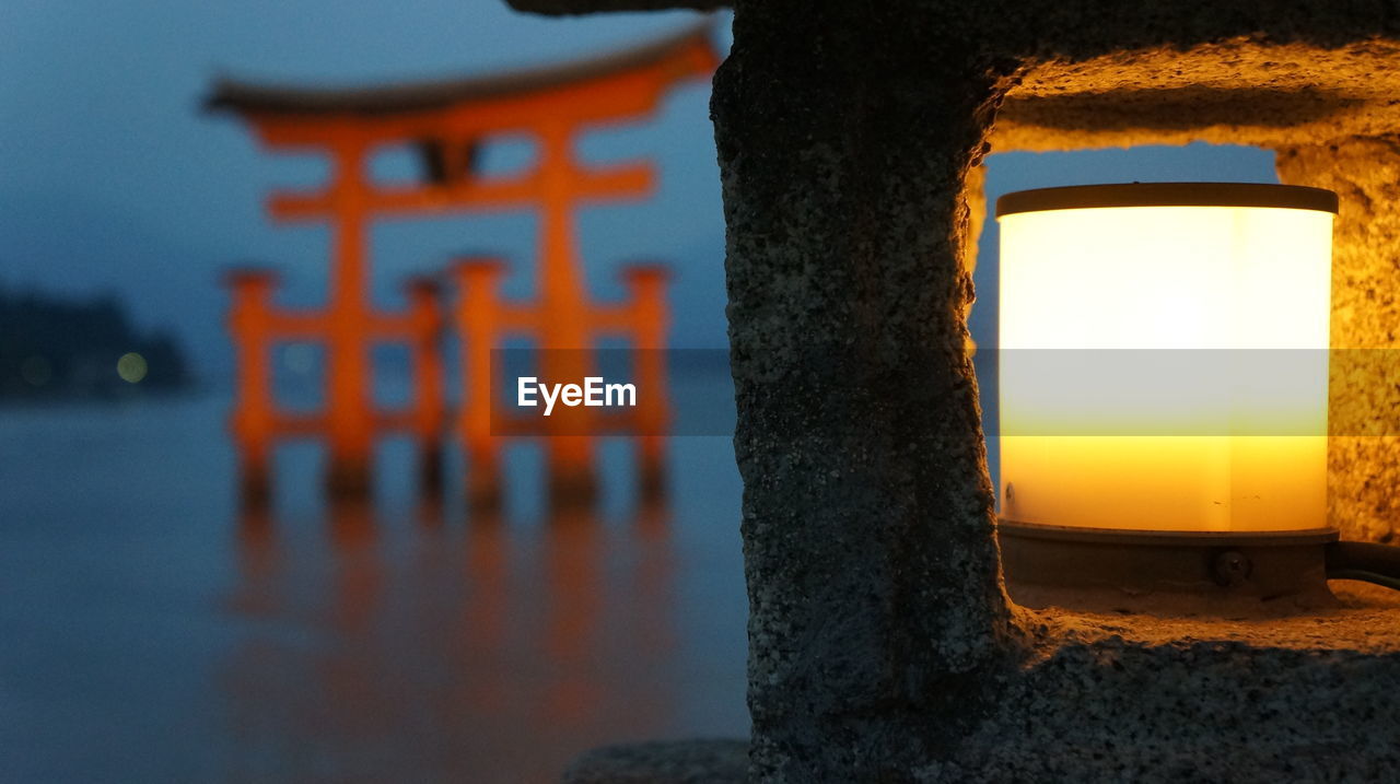 Illuminated gas light in front of itsukushima shrine torii gate during twilight