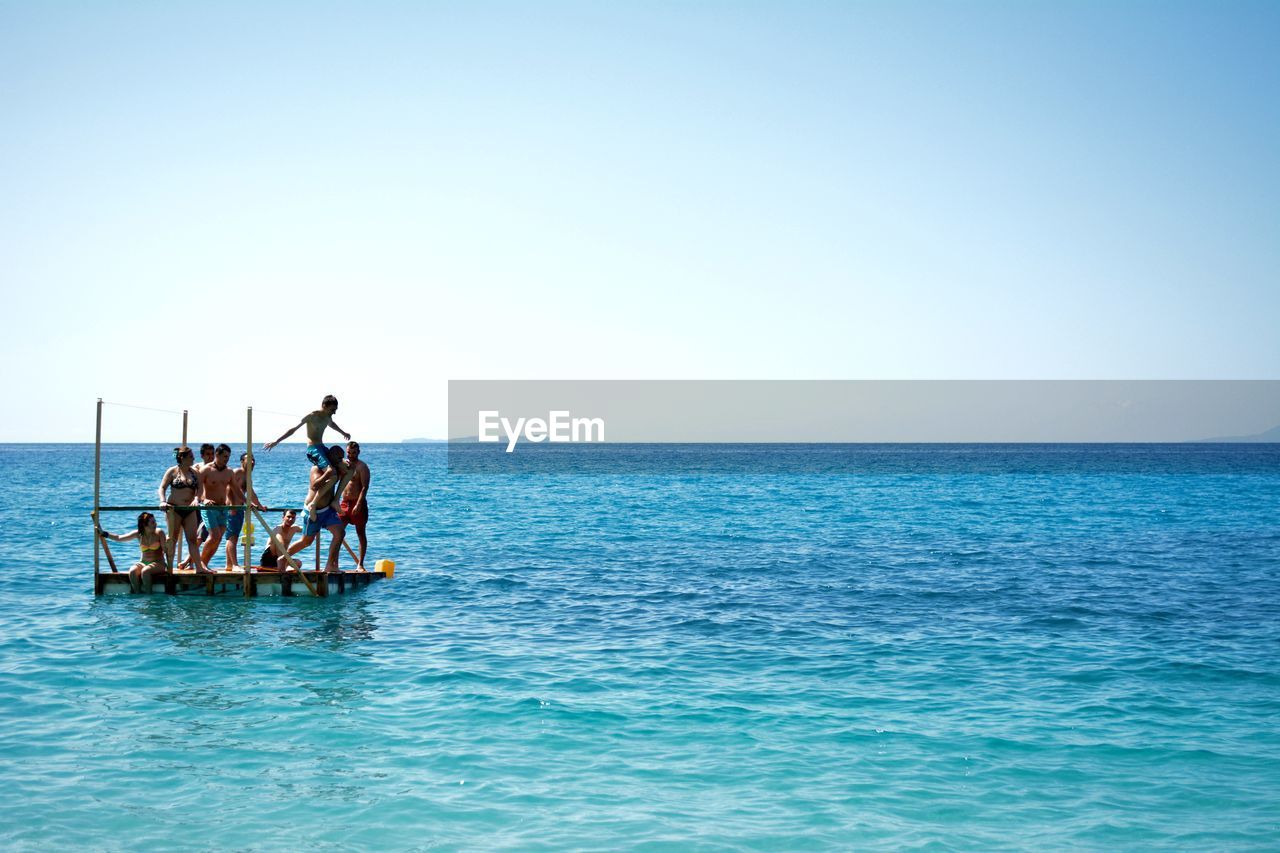 Friends on diving platform in sea against clear sky