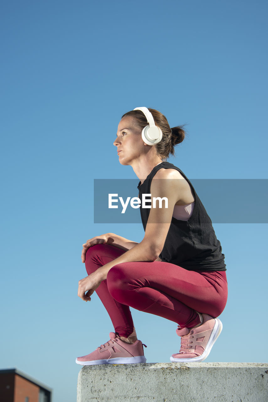 Woman wearing headphones and listening to music outside in the sun, urban setting.