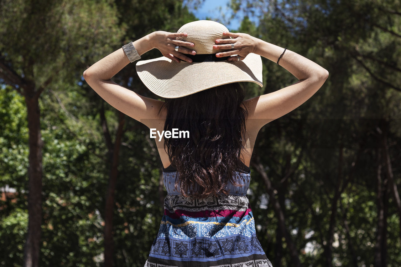 Rear view of woman wearing hat standing against trees