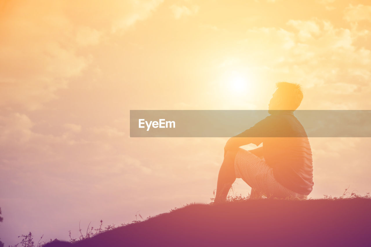 Side view of silhouette man sitting against sky during sunset