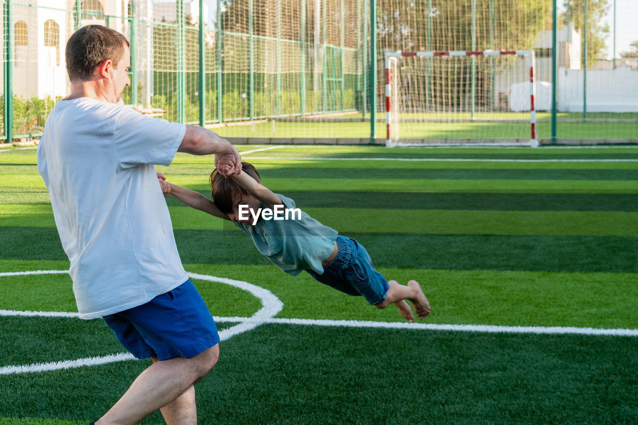 Father spinning son on sports ground. view from behind