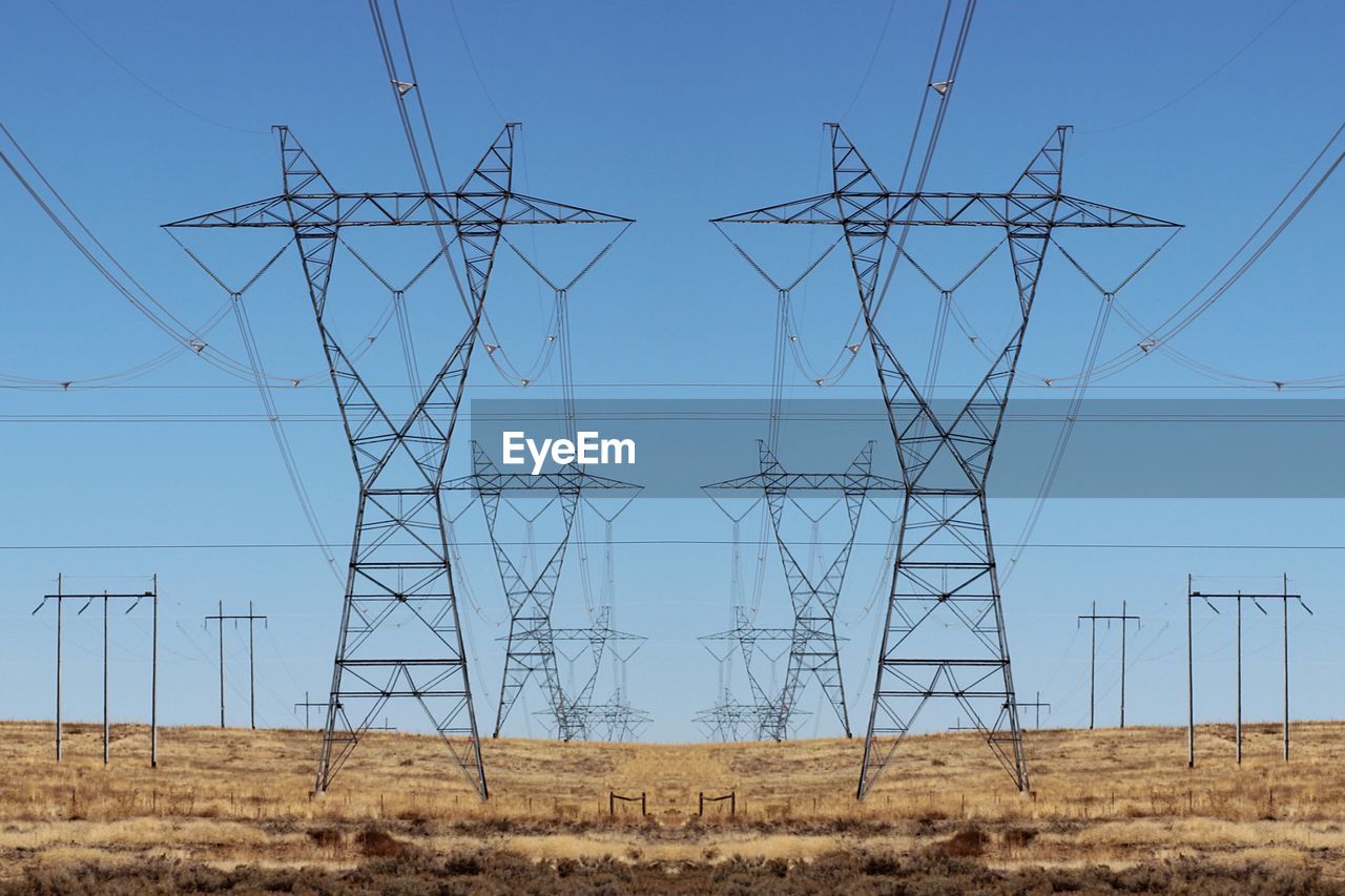 Low angle view of electricity pylon on field against clear blue sky