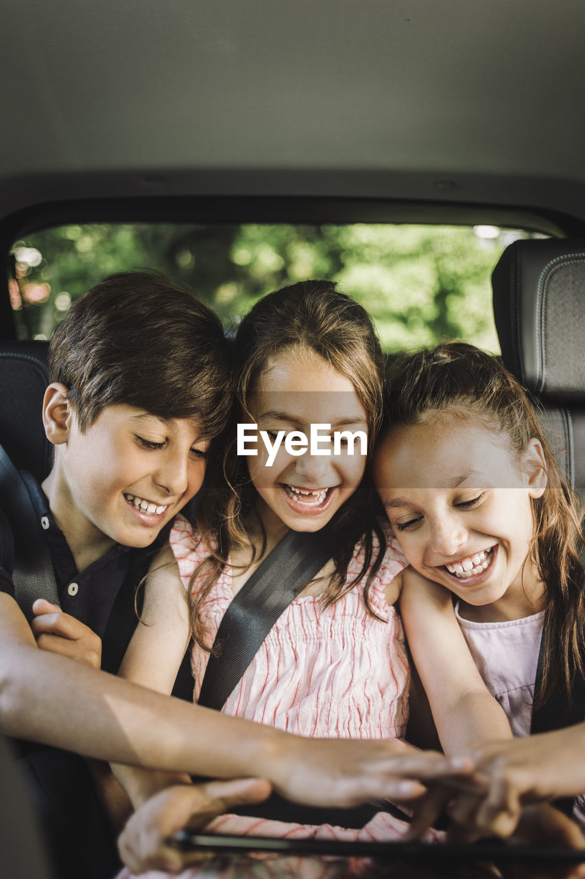 Happy siblings sharing tablet pc while while traveling in car