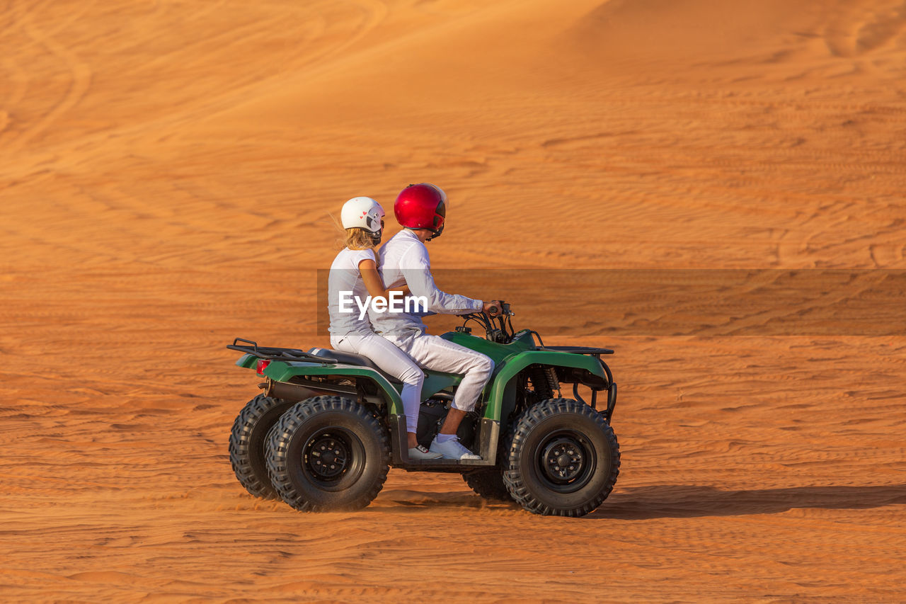 Side view of couple on quadbike at desert