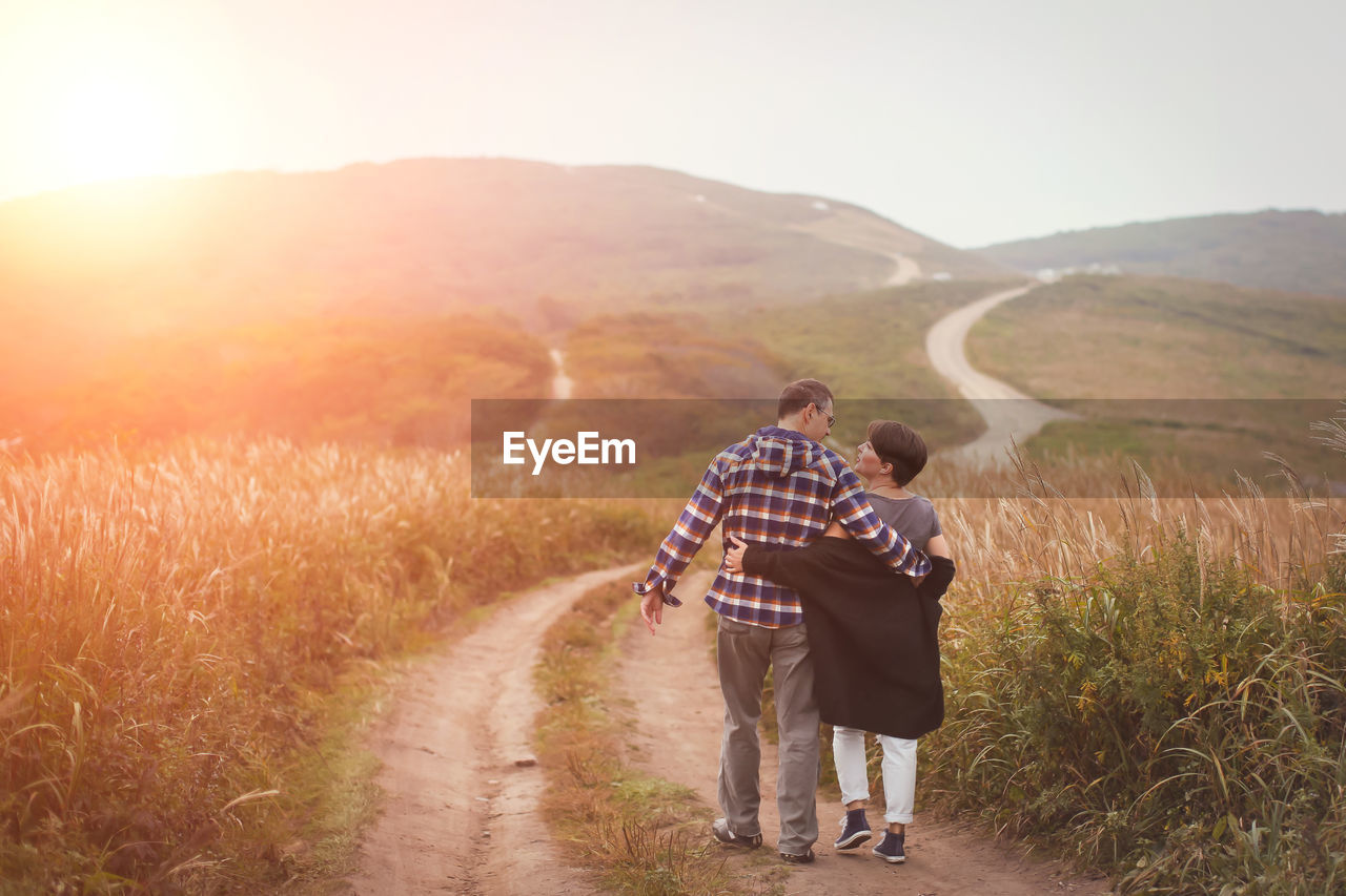 Rear view full length of couple walking on mountain road