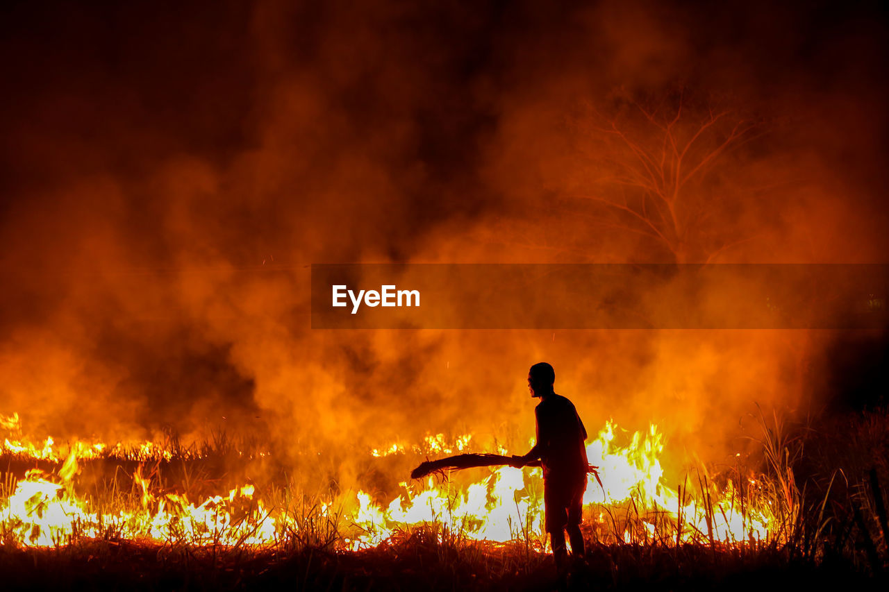 Silhouette man standing by fire at night