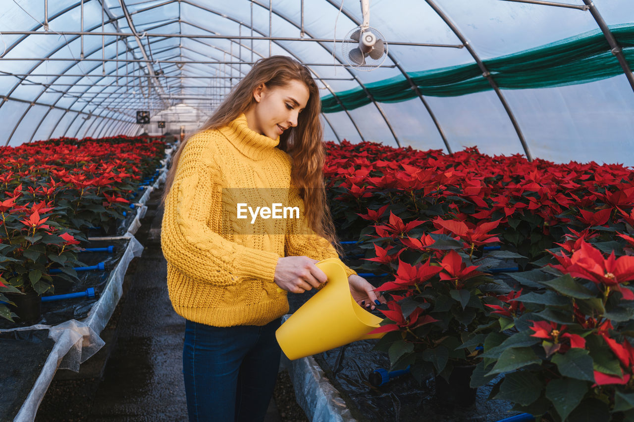 BEAUTIFUL YOUNG WOMAN STANDING BY FLOWERING PLANT