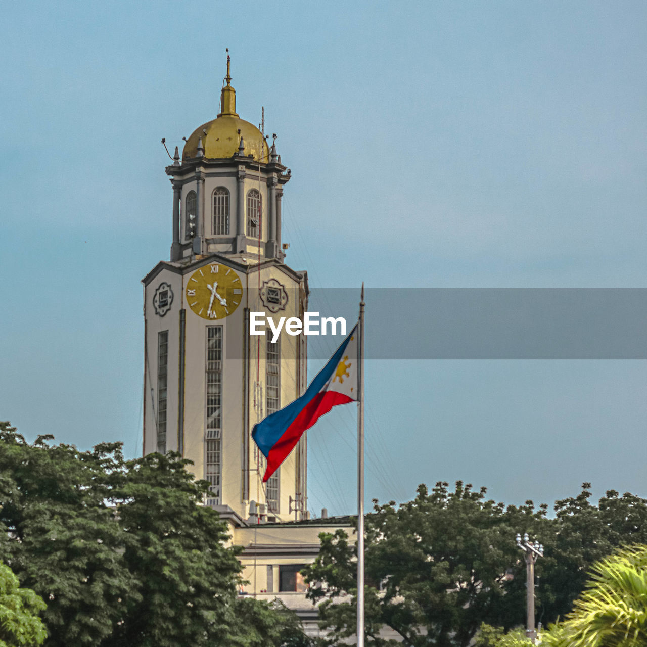 architecture, built structure, building exterior, clock, landmark, flag, tree, tower, sky, nature, patriotism, building, travel destinations, plant, no people, clock tower, day, steeple, religion, history, place of worship, outdoors, the past, low angle view, bell tower, travel, city, time, belief, blue, tourism