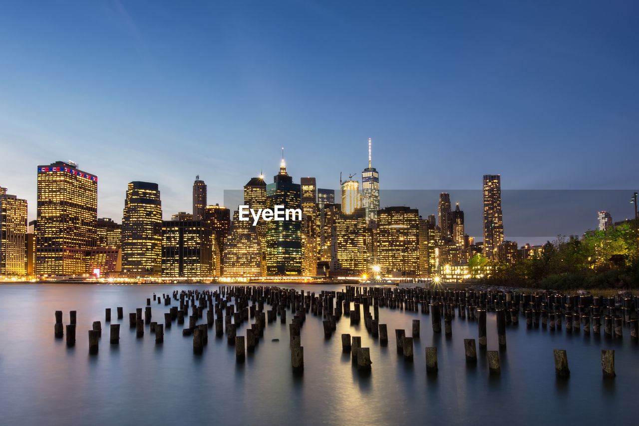 Wooden posts in river against sky in city at night