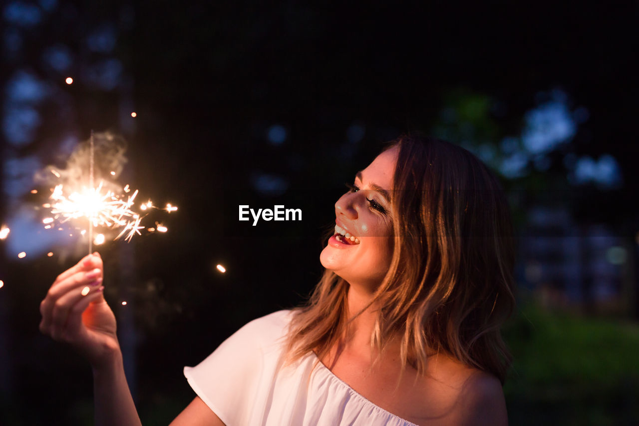 Smiling woman with sparklers at night