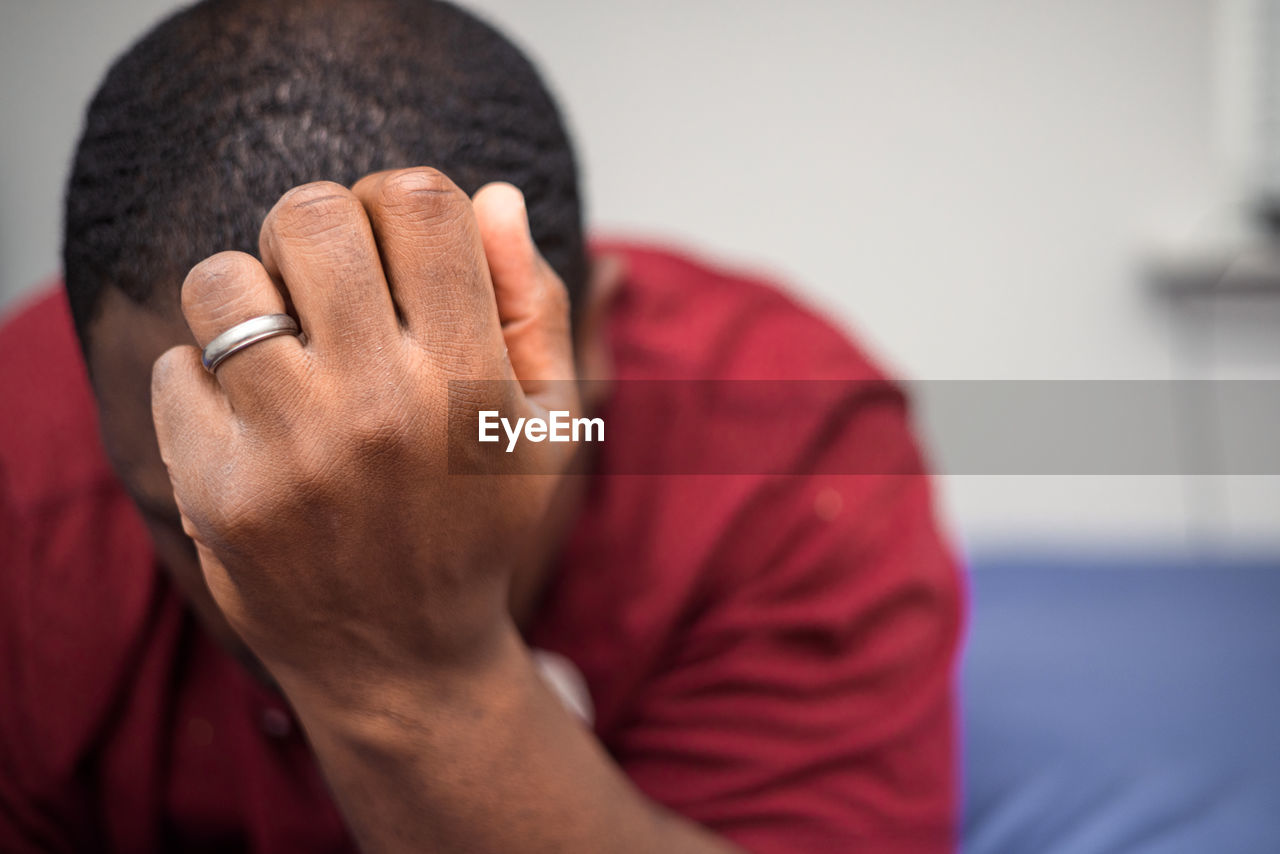 Young depressed or anxious african american man in bedroom at home sitting