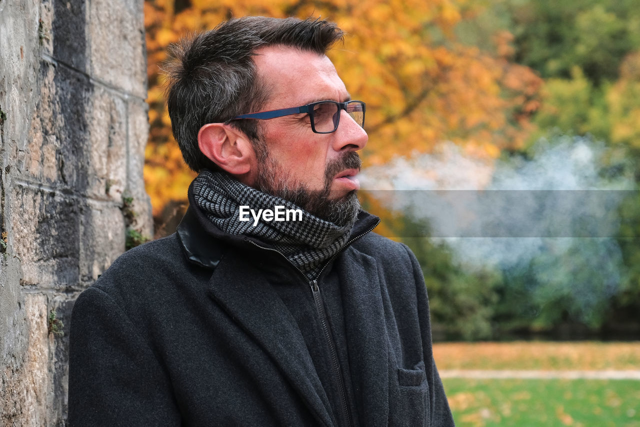Mature man smoking cigarette standing against trees