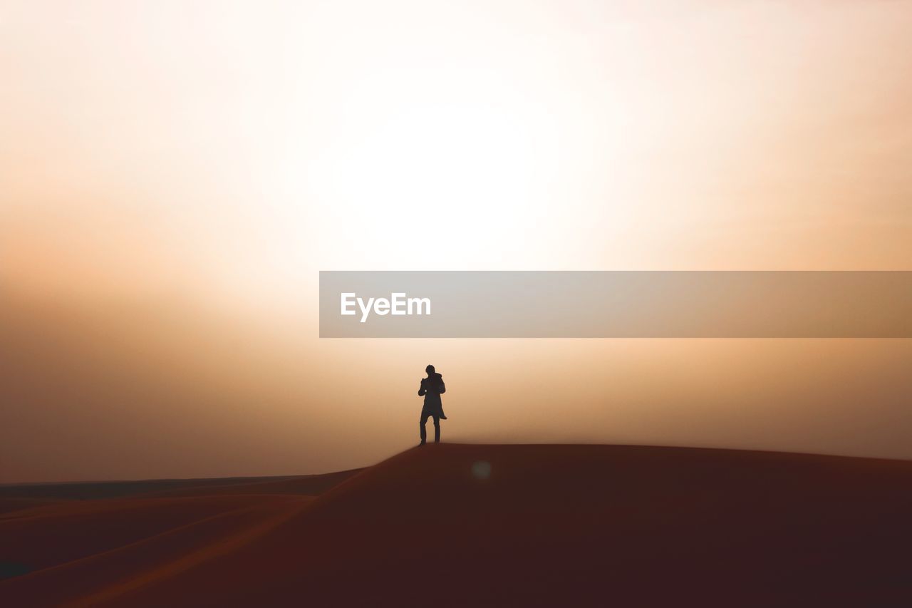 Silhouette woman standing at desert against sky during sunset