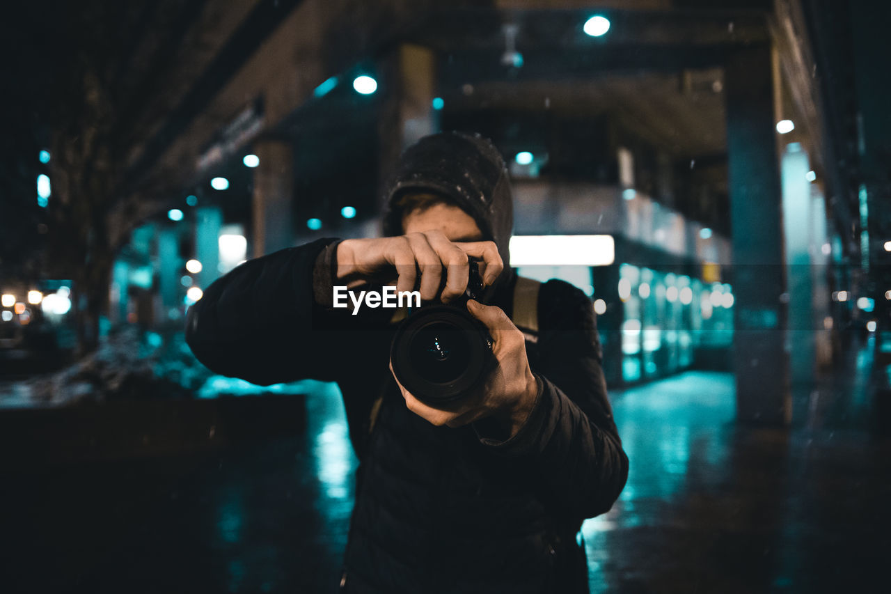 MAN PHOTOGRAPHING AT ILLUMINATED CITY