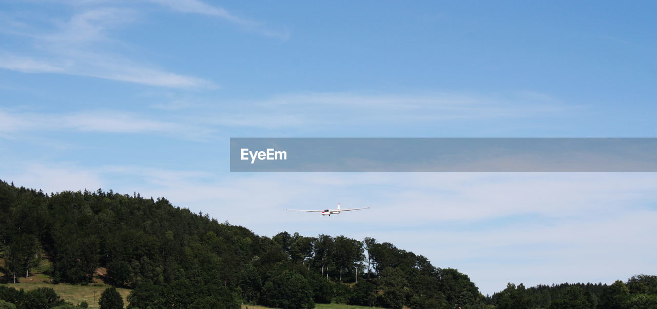 Glider on a background of the blue sky in the mountains flying over the trees