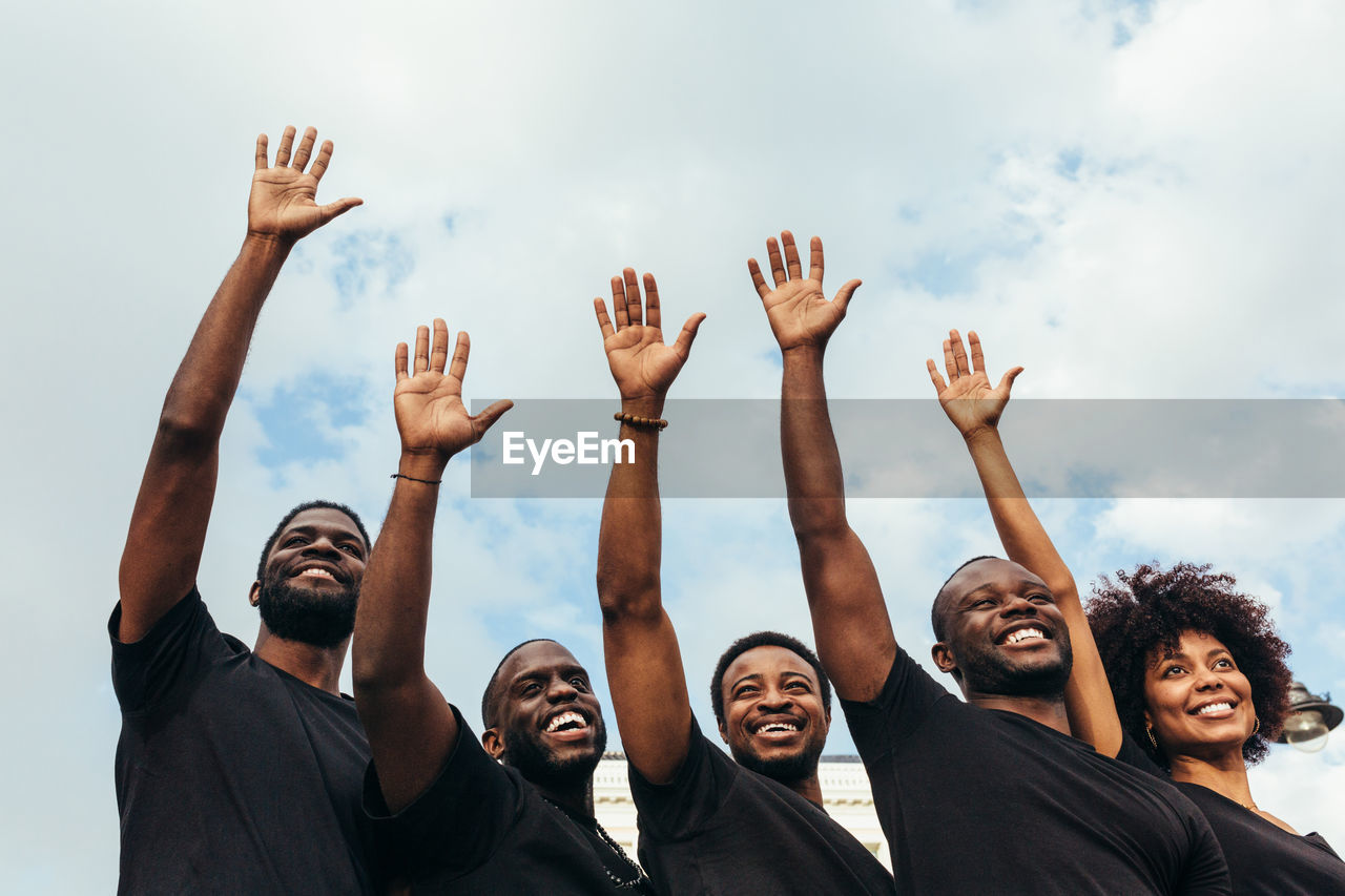 Cheerful black men and woman raising hands against a blue sky