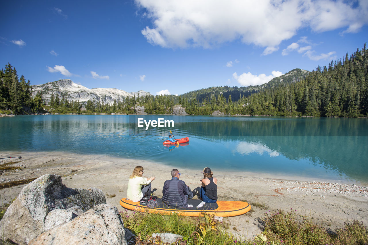 Family relaxing together at remote lake, brother paddling on lake.