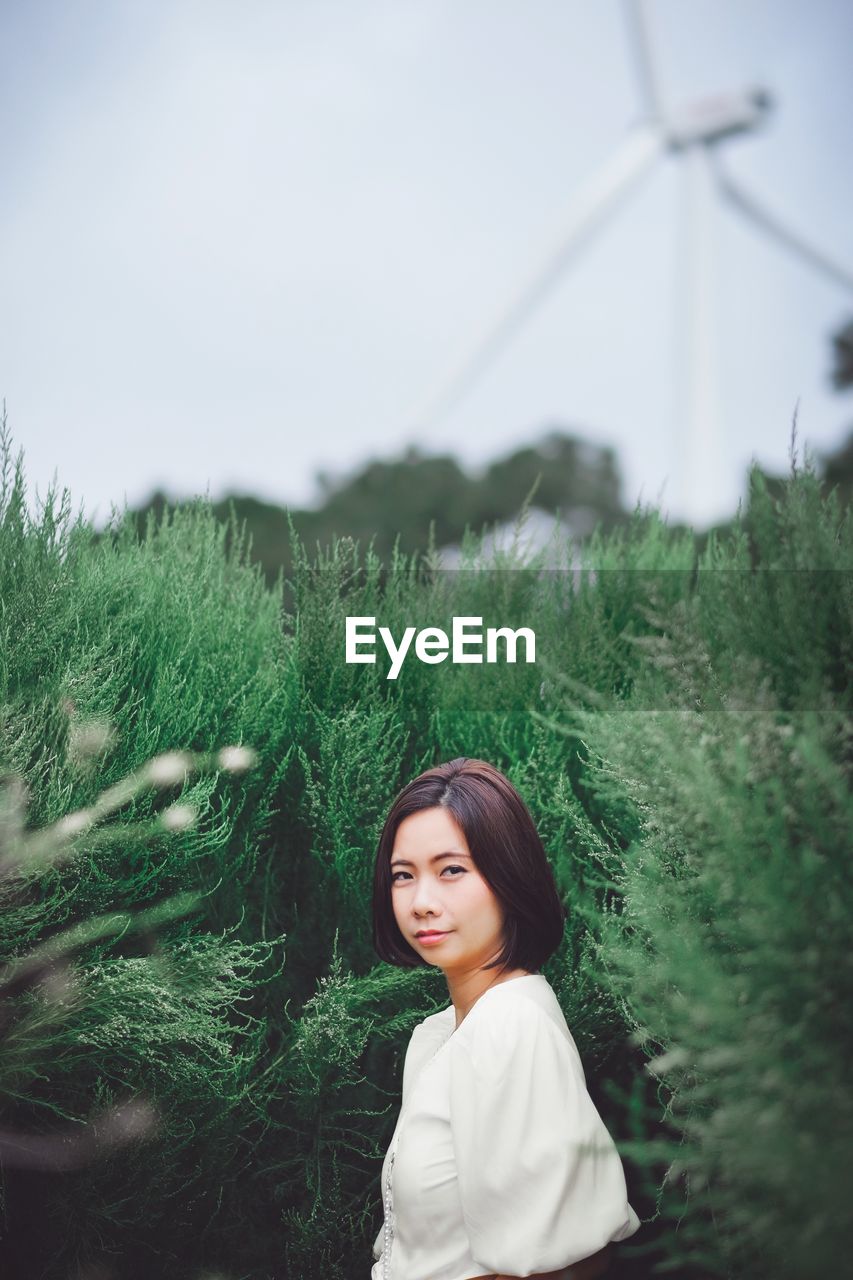 Portrait of woman standing amidst plants against clear sky