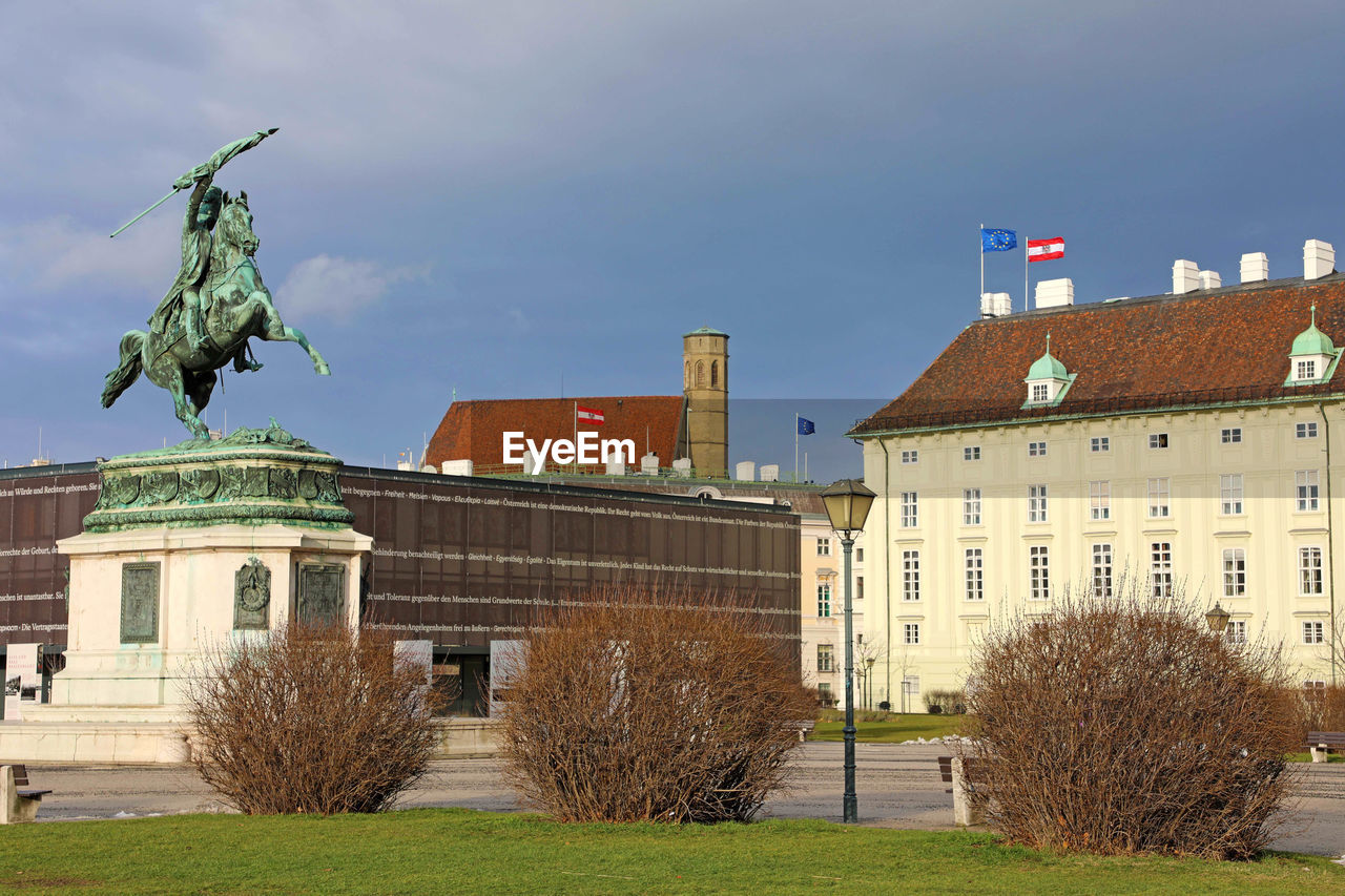 STATUE AMIDST BUILDINGS AGAINST SKY