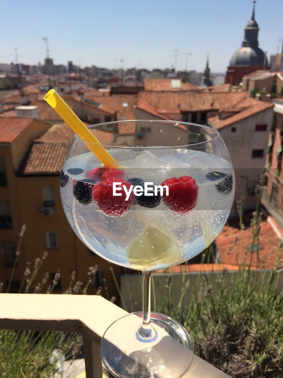 Close-up of drink on railing at balcony against buildings