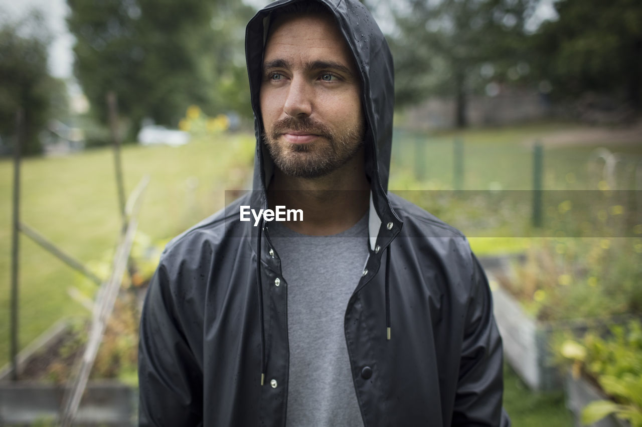 Thoughtful mid adult man wearing raincoat in vegetable garden