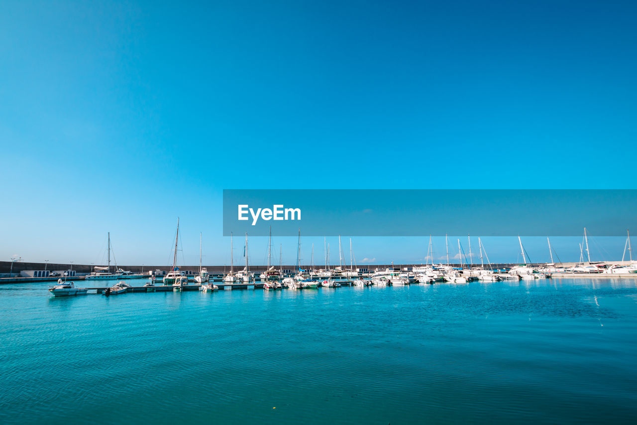 BOATS MOORED IN SEA AGAINST BLUE SKY