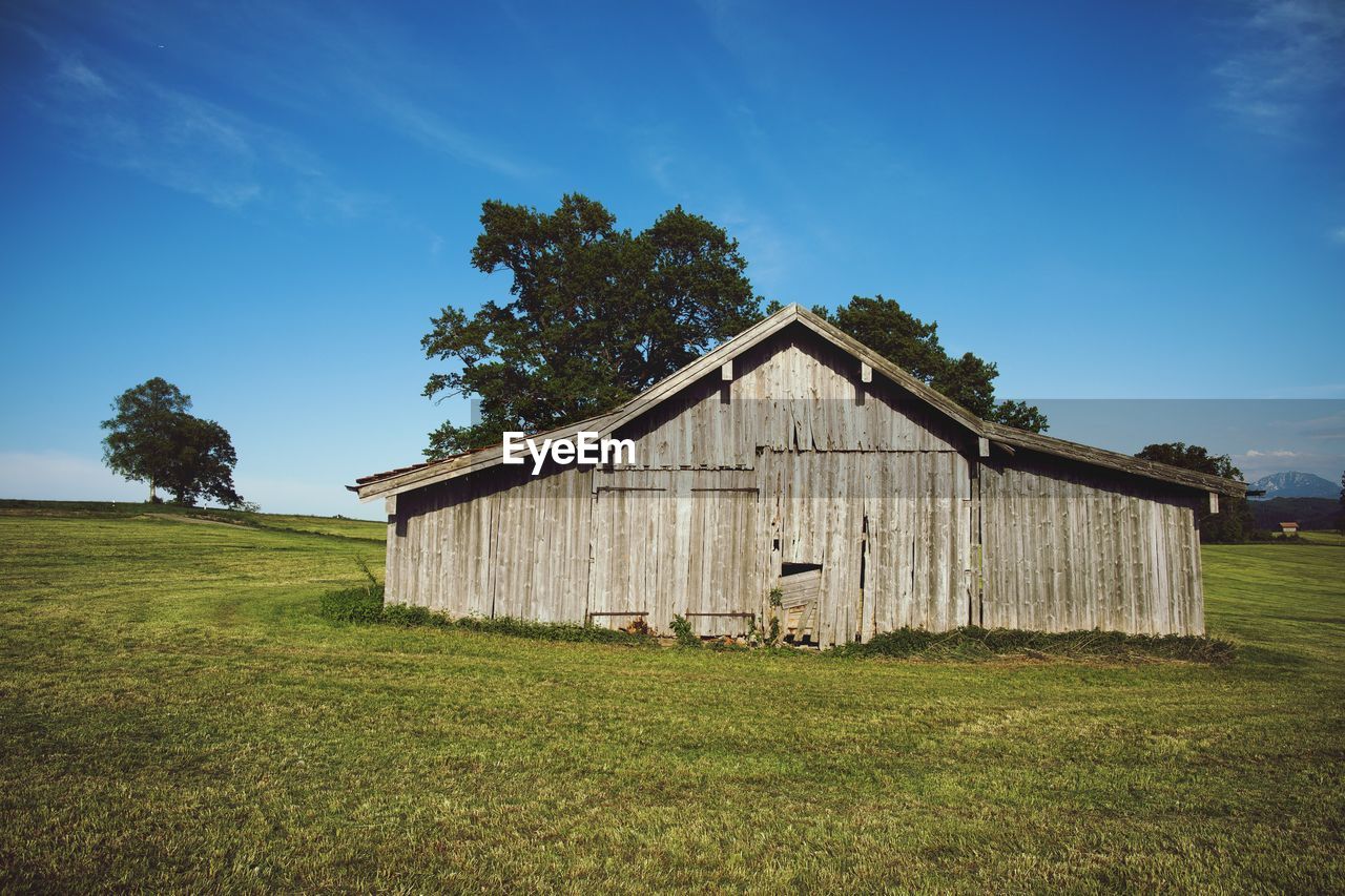 BARN ON GRASSY FIELD AGAINST SKY